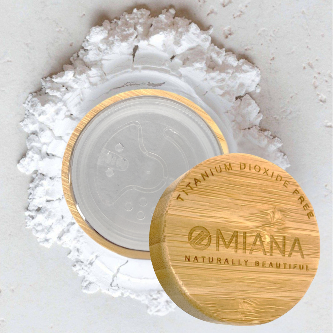 Omiana Mineral Veil finishing powder titanium dioxide-free mineral makeup in  Bamboo container with white powder behind the container on a white background with wooden cap on a light background